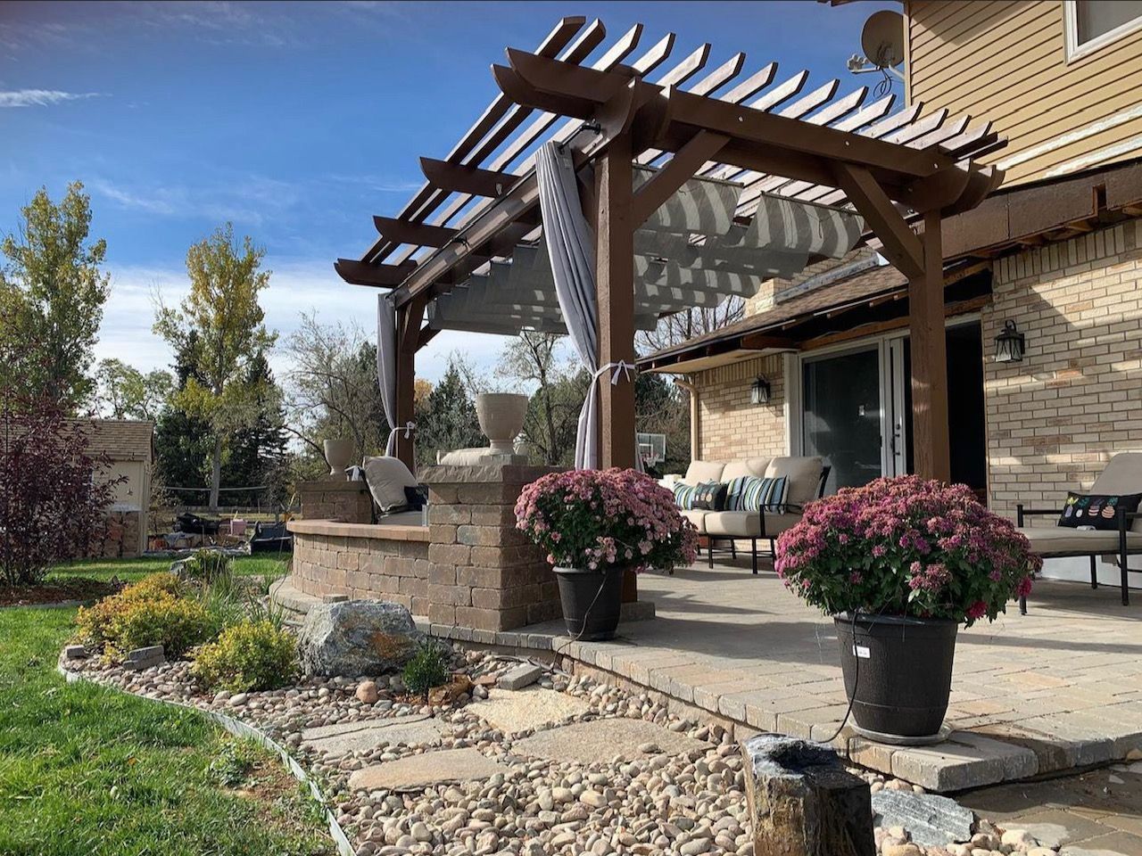 Front yard garden with stone path, pergola, and potted pink flowers beside a house