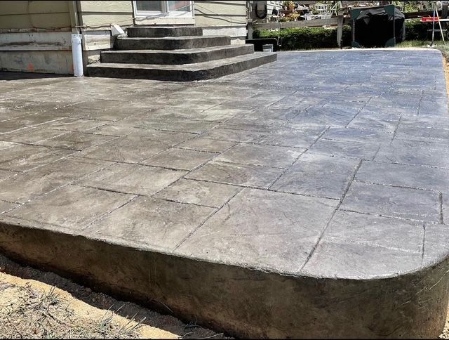 Stamped concrete patio with rounded front edge beside house steps and a yard