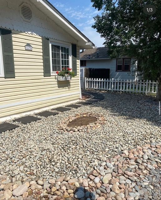 House exterior with white siding, gravel yard, and a small window flower box near a picket fence.