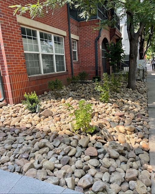Brick building with large window beside a sidewalk landscaped with smooth river rocks and small plants