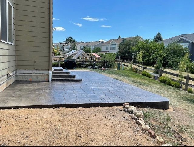 Backyard patio with dark tile, house siding, and a dirt yard bordered by rocks and a fence