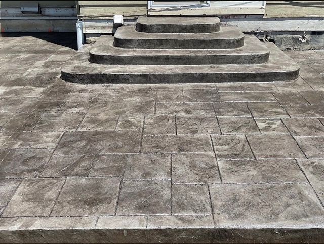 Concrete steps leading up to a raised stone platform on a tiled courtyard.