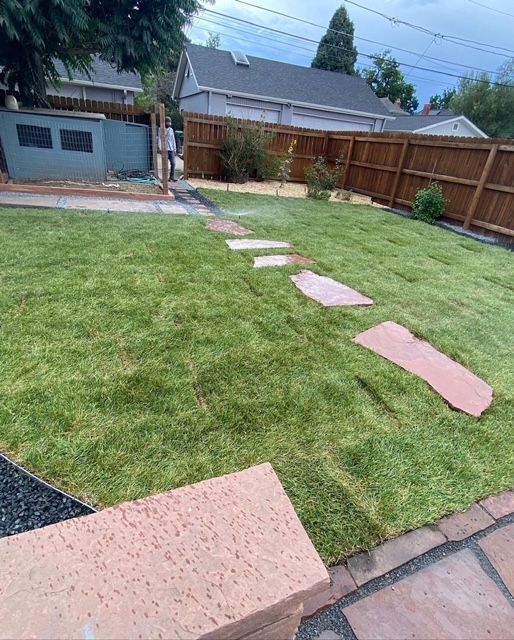 Backyard lawn with pink stepping stones leading to a fence and garage under a cloudy sky