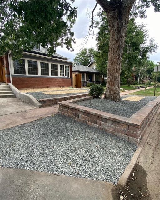 Brick house with gravel landscaping, raised planter, and large tree in front yard